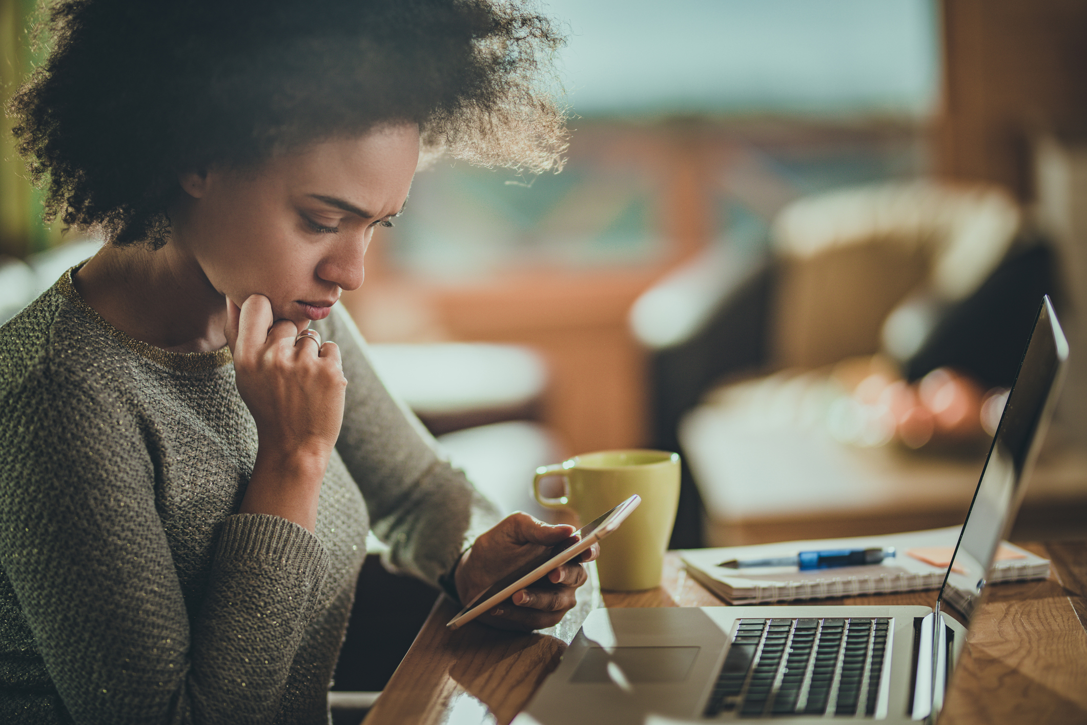 Worried African American woman using cell phone while working at home.