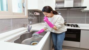 Mujer tapándose la nariz, mientras lava el lavaplatos (Getty Images)